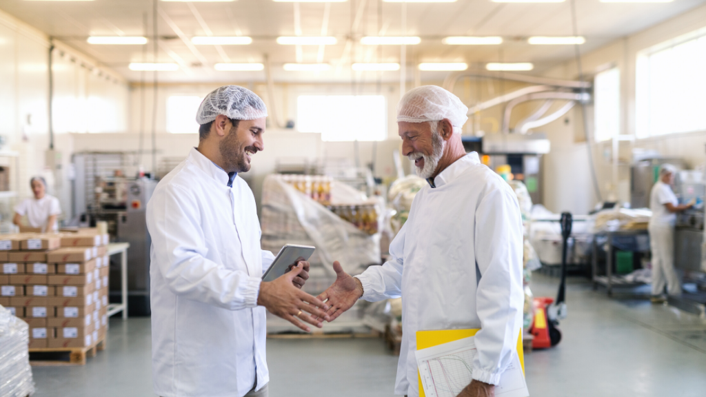 Two businessmen shaking hands while standing in food factory.